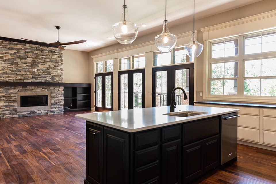 A Superior Homes custom build: kitchen with a dark island, glass globe pendants and a stacked-stone fireplace beyond